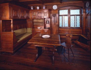 Room from the Villa Solitude; a:  Room (panel, windows, built-in cabinets & seat, 50 books in locked case); b: Table; c-d: two chairs; e: cradle; f: bread board with cutter; i: basin; j: watercan; k: candlestick; l: chandelier.