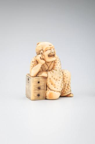 Netsuke: man resting right elbow on three-drawer chest